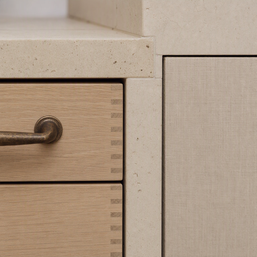 Close detail of honed limestone, pale oak joinery, natural linen, and aged bronze hardware