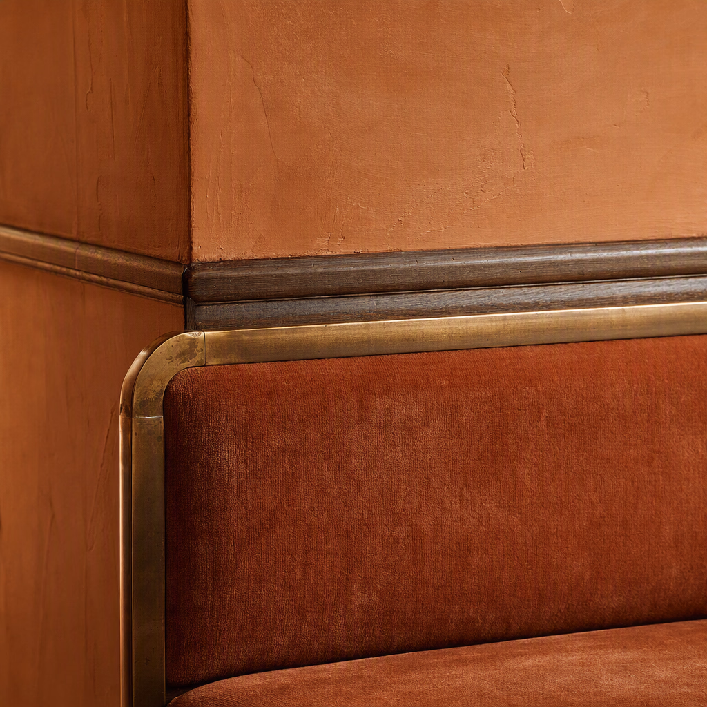 Close detail of rust-colored mohair, dark oak, pigmented plaster, and aged brass trim